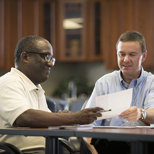 Two men sitting at a desk talking.