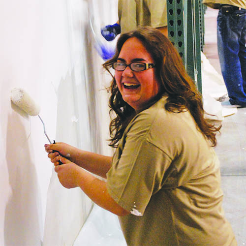 A smiling woman painting a wall with a paint roller. 