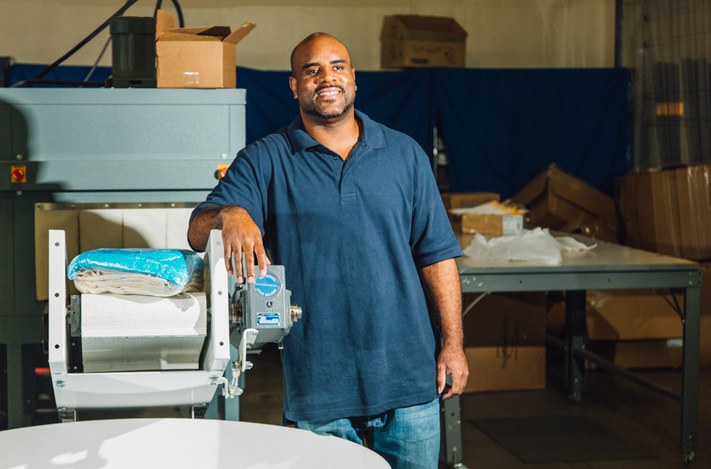 A man leaning against a production machine smiling at the camera