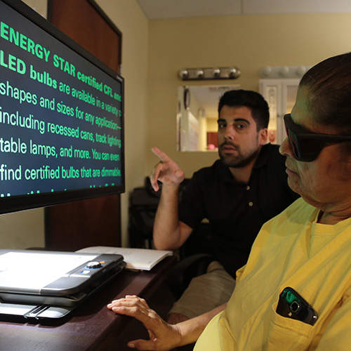 Man teaching a woman to use monitor with large type.