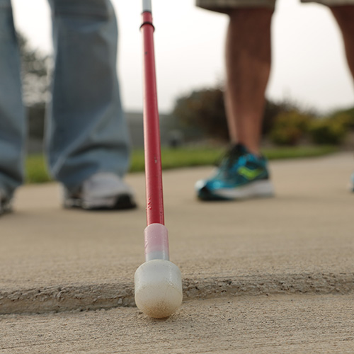 A closeup of a white cane being used on a sidewalk.