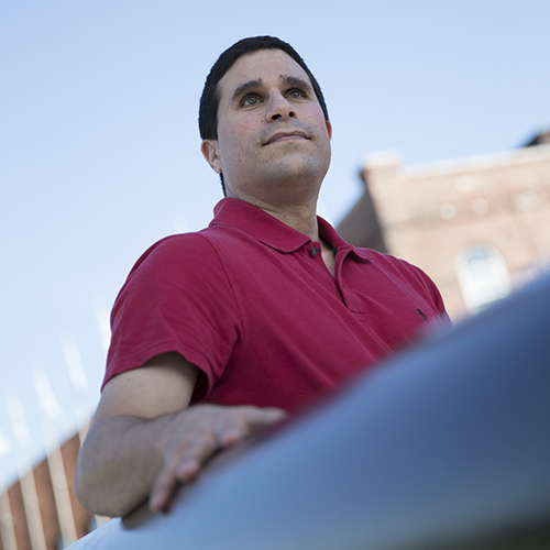 A man outside with his hand on a handrail looking off into space.