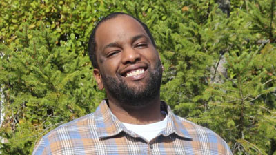 Ory Watson standing in a park smiling at the camera holding a white cane.