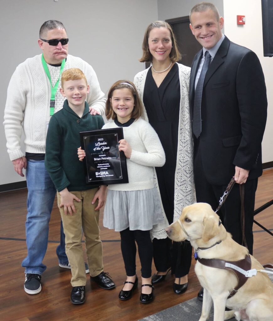Brian Petraits receiving his award while standing with his family and Jeff Mittman