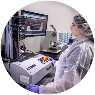 Woman wearing personal protective equipment standing in front of testing equipment