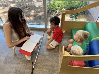 Blind woman reading braille book while two children listen.