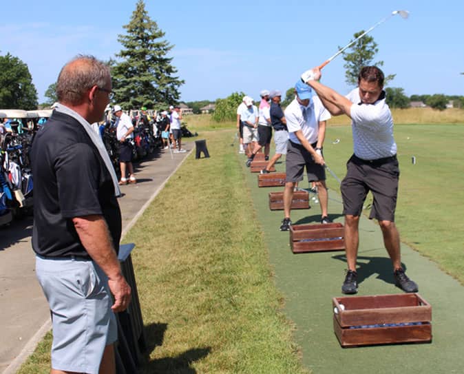 Group of golfers warming up with practice swings on a driving range.