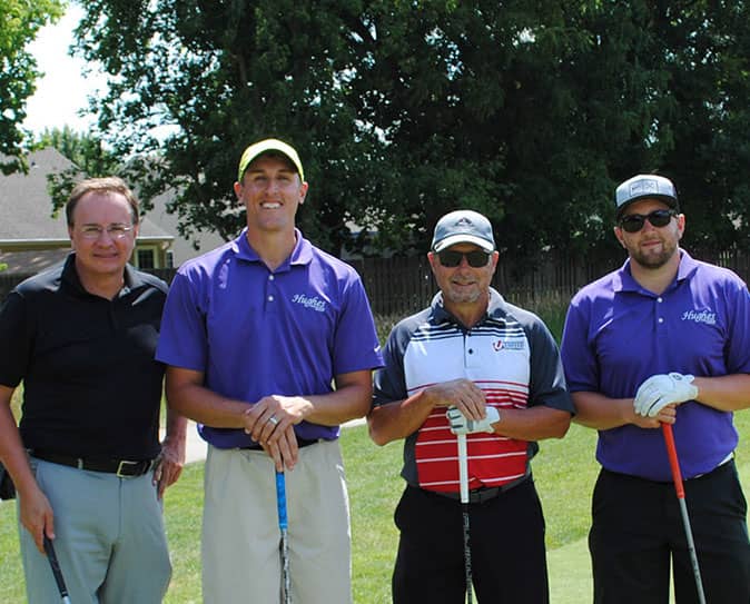 A golf foursome holding their putters and smiling at the camera