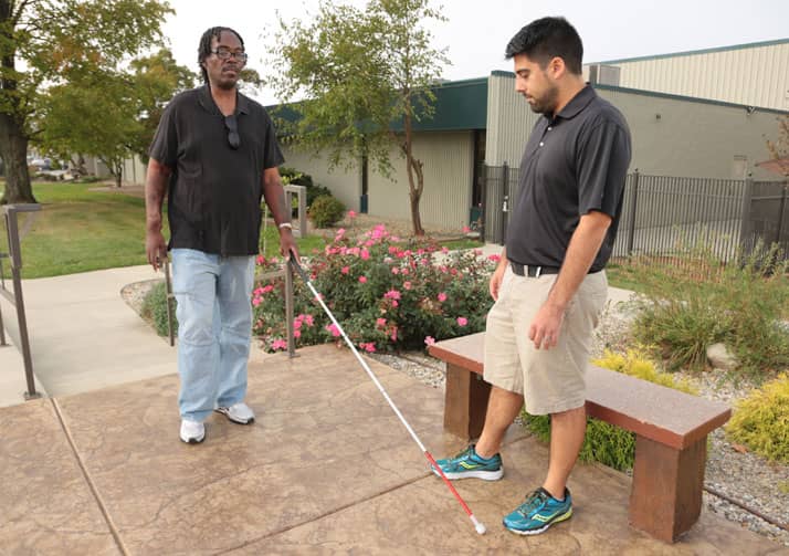 Bosma trainer helping man learn to navigate sidewalk with white cane.
