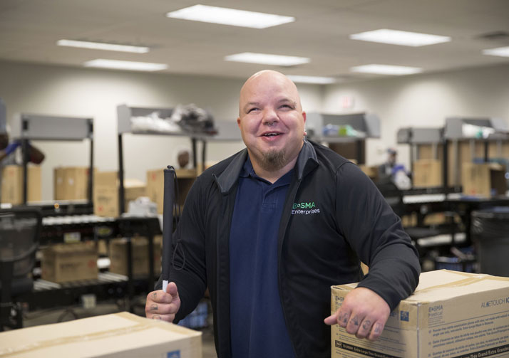 Man standing in box packing area, smiling at camera.