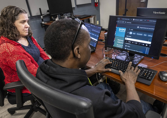Man and woman sitting at desk working on computer together.