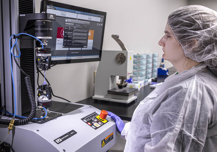 Woman wearing personal protective equipment standing in front of testing equipment