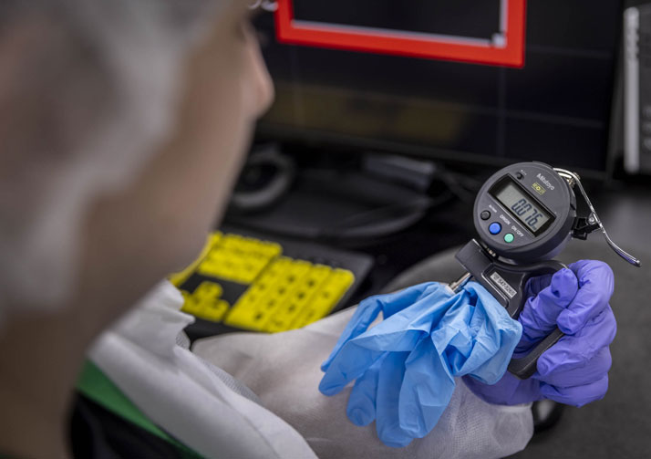 Woman wearing personal protective equipment using testing equipment to examine gloves.