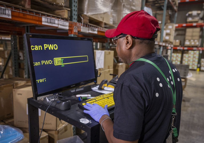 Man working at computer in warehouse entering data.