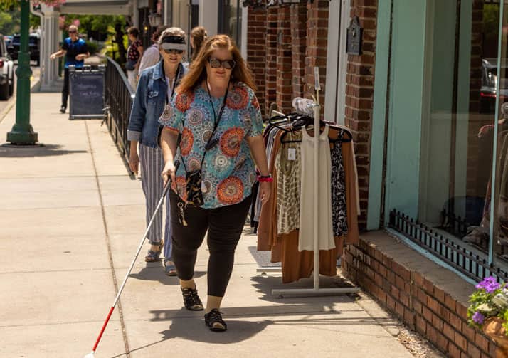 Two women walking on sidewalk outside of shops.